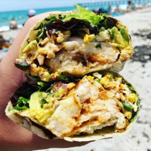 A chicken wrap in someone's hand on the beach.